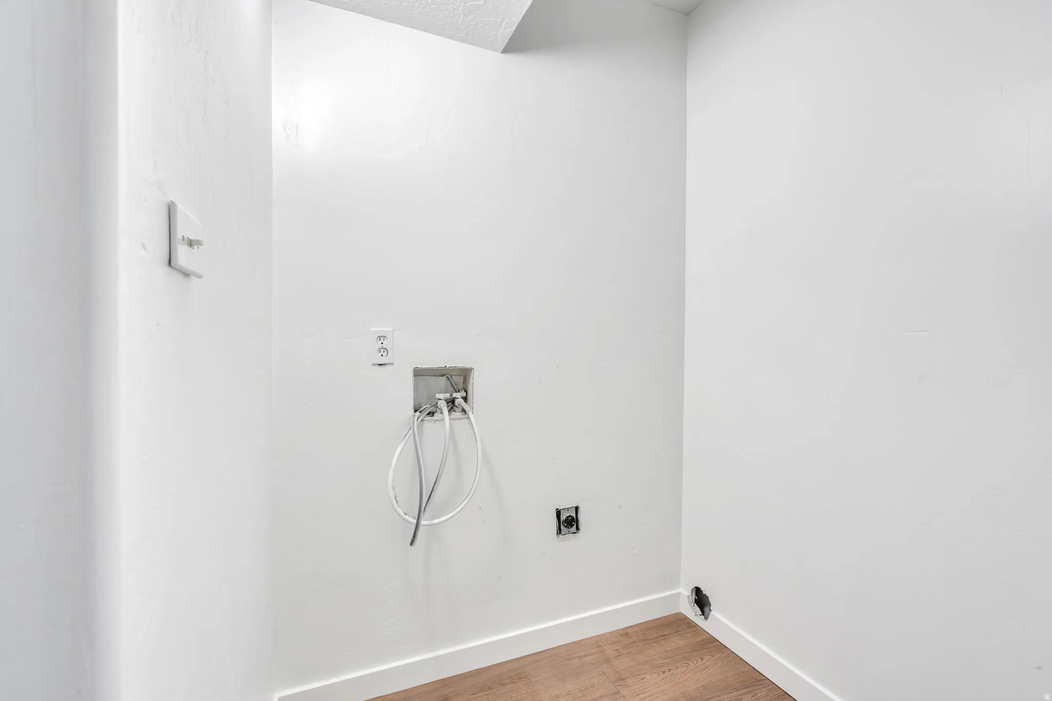 Dedicated laundry area featuring a water hookup, electrical outlet, and wood-finish flooring