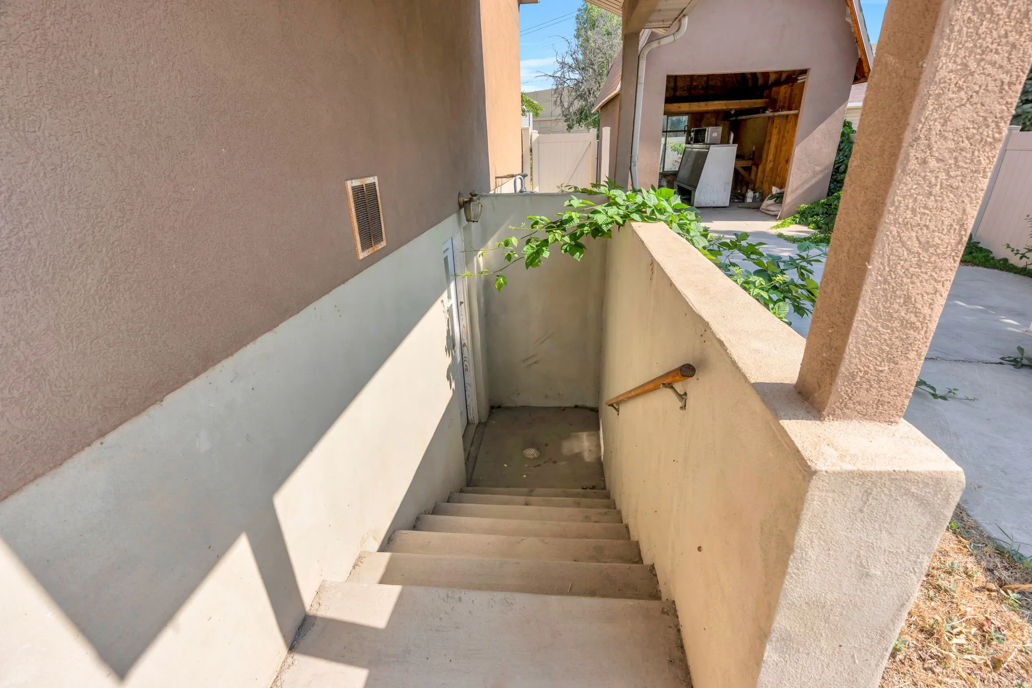 Concrete exterior stairway with a wood-finish handrail, leading to a lower-level entry