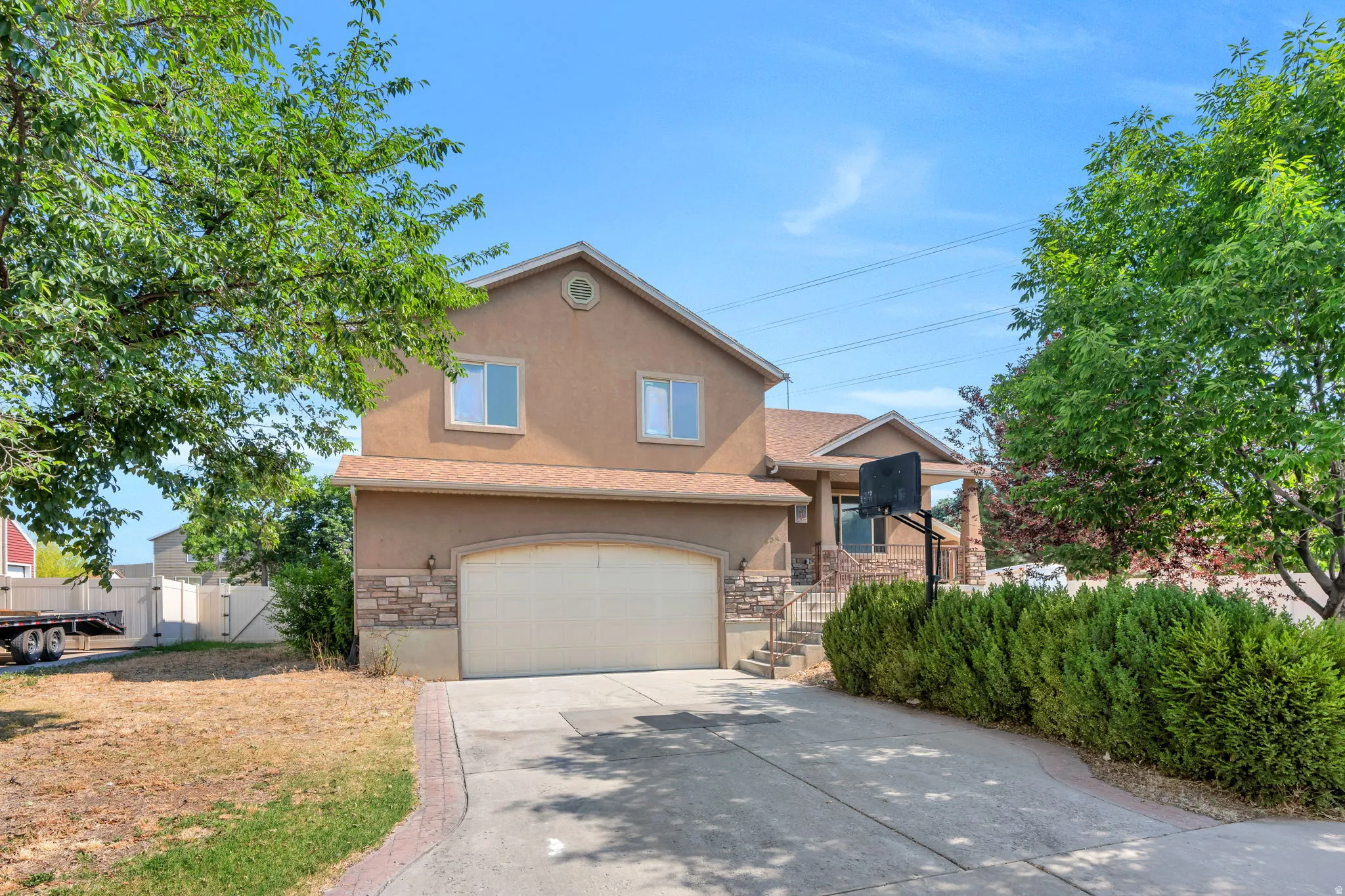 Stucco exterior residence featuring a stone accent façade, an arched garage door, a covered front porch, and a paved driveway with brick edging