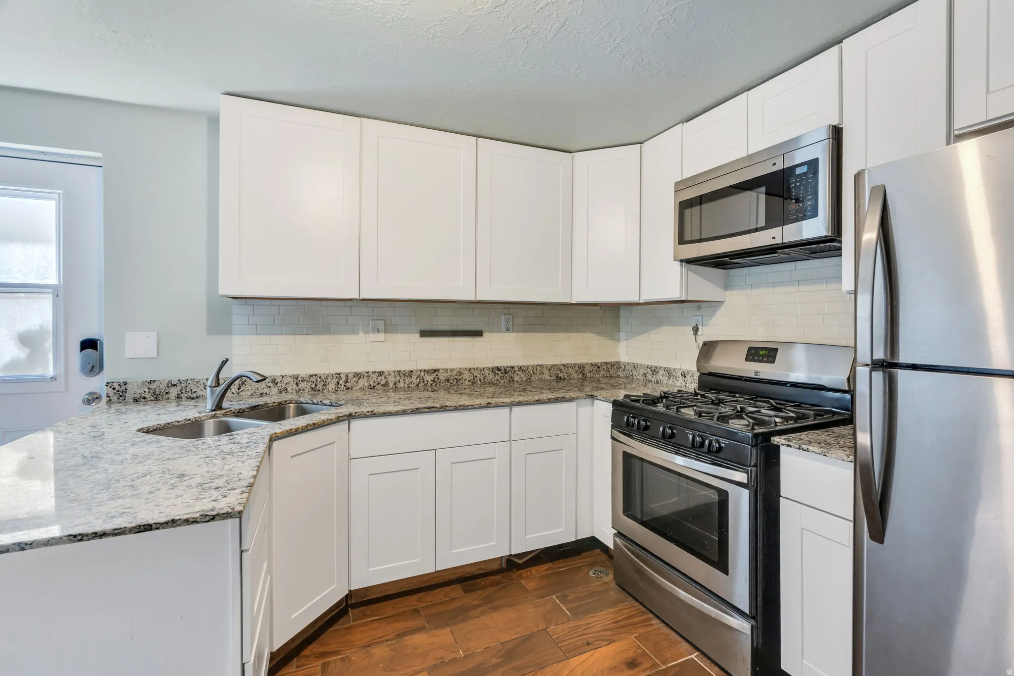 Kitchen featuring white cabinetry, granite countertops, stainless steel appliances, tile backsplash, and wood-finish flooring