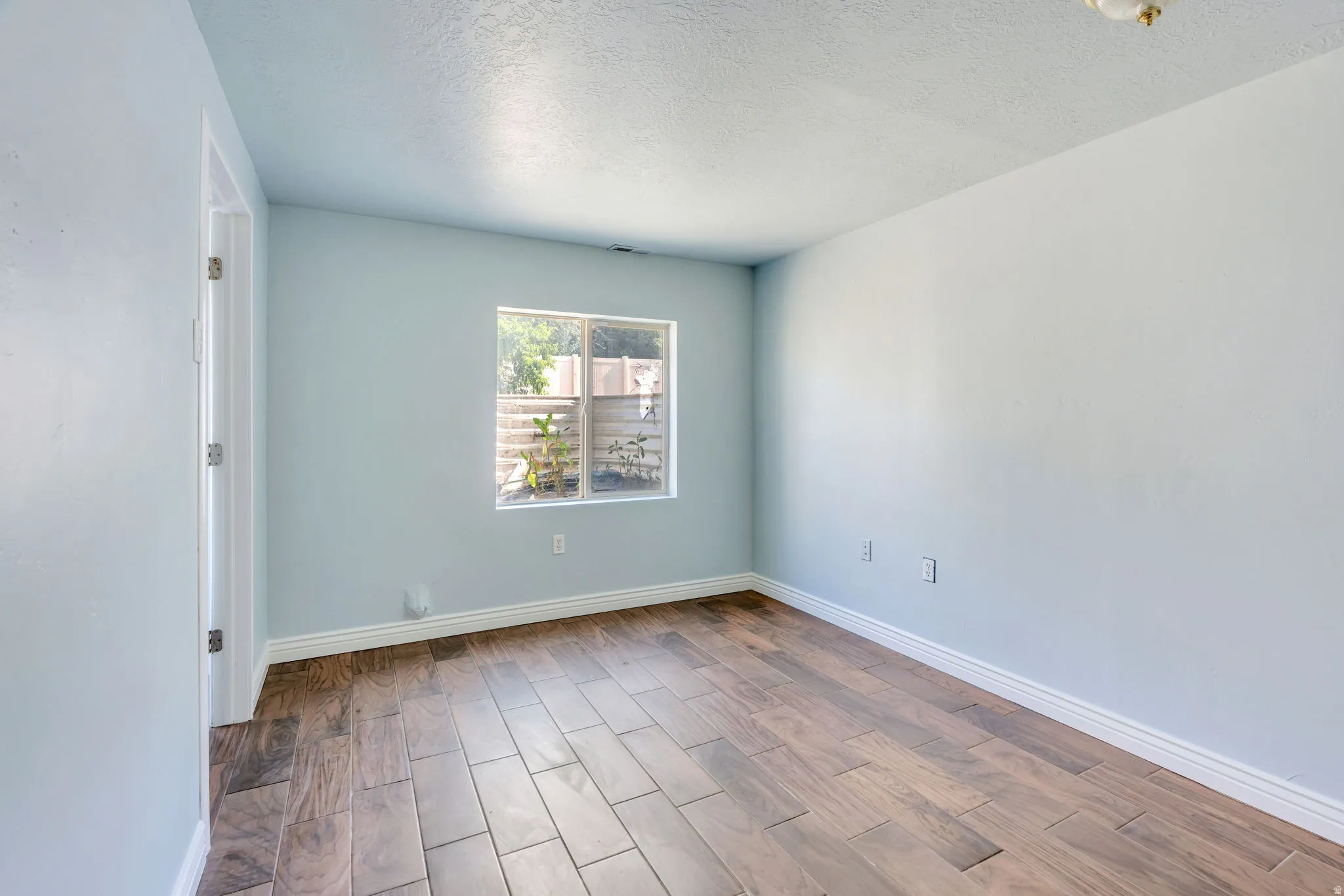 Bright room featuring wood-finish flooring, light blue wall paint, white baseboards, a single window, and a white ceiling