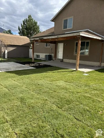 Rear exterior featuring a covered patio, concrete hardscaping, leveled sod lawn, and detached structure