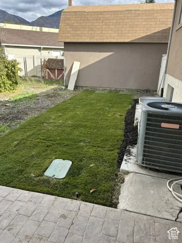Exterior area featuring a paved stone patio, fresh sod lawn, and an external HVAC unit, set against a mountain backdrop