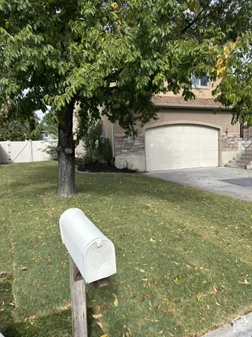 Exterior facade featuring stone veneer detailing, a multi-car garage, concrete driveway, and established tree within the lawn