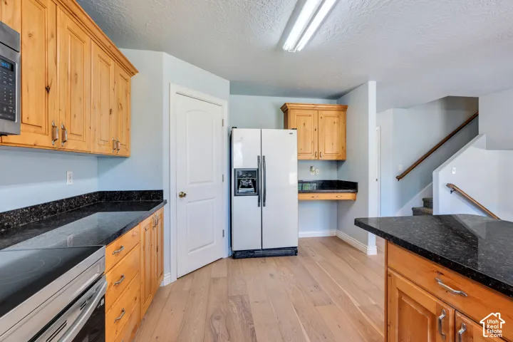 Kitchen featuring wood cabinetry, dark granite countertops, wood-finish flooring, and stainless steel appliances