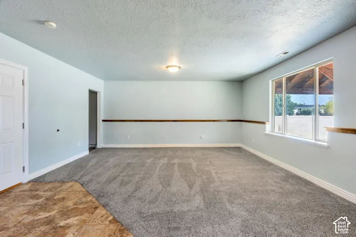 Spacious room featuring light blue walls, gray textured carpeting, and a large window with white trim