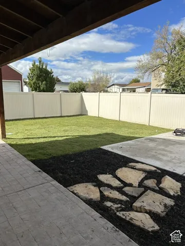 Backyard featuring a privacy fence, stone paver patio, manicured lawn, and decorative stone accent area