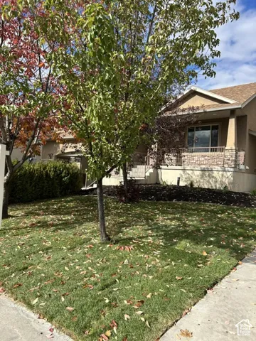 Stucco exterior featuring a stone-veneer porch base, covered front entrance, metal railing, and manicured lawn