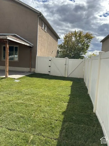 Backyard featuring a grass lawn, white vinyl fencing, double gate access, and a concrete patio