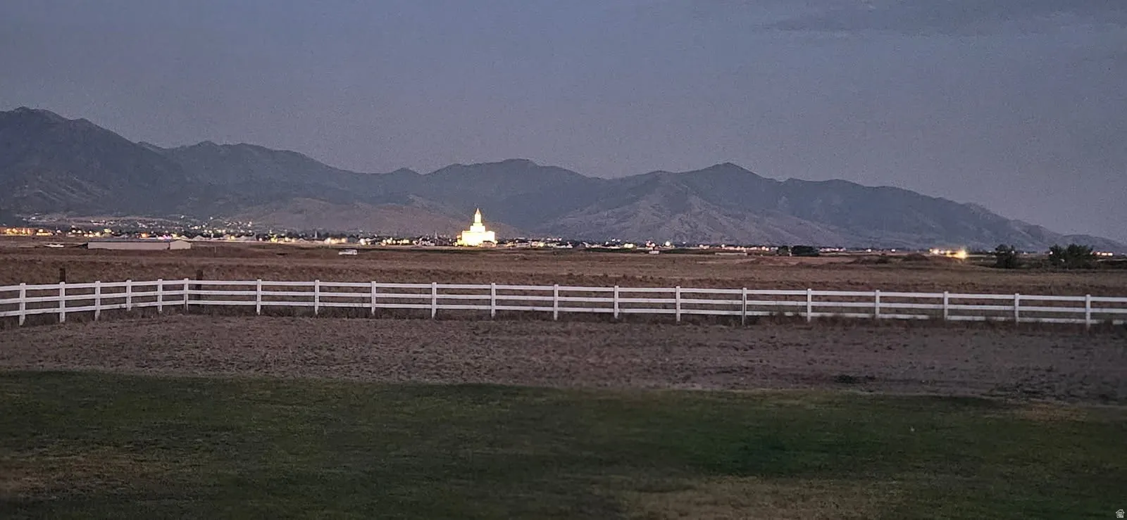 Expansive open land with a white three-rail fence, offering distant mountain scenery