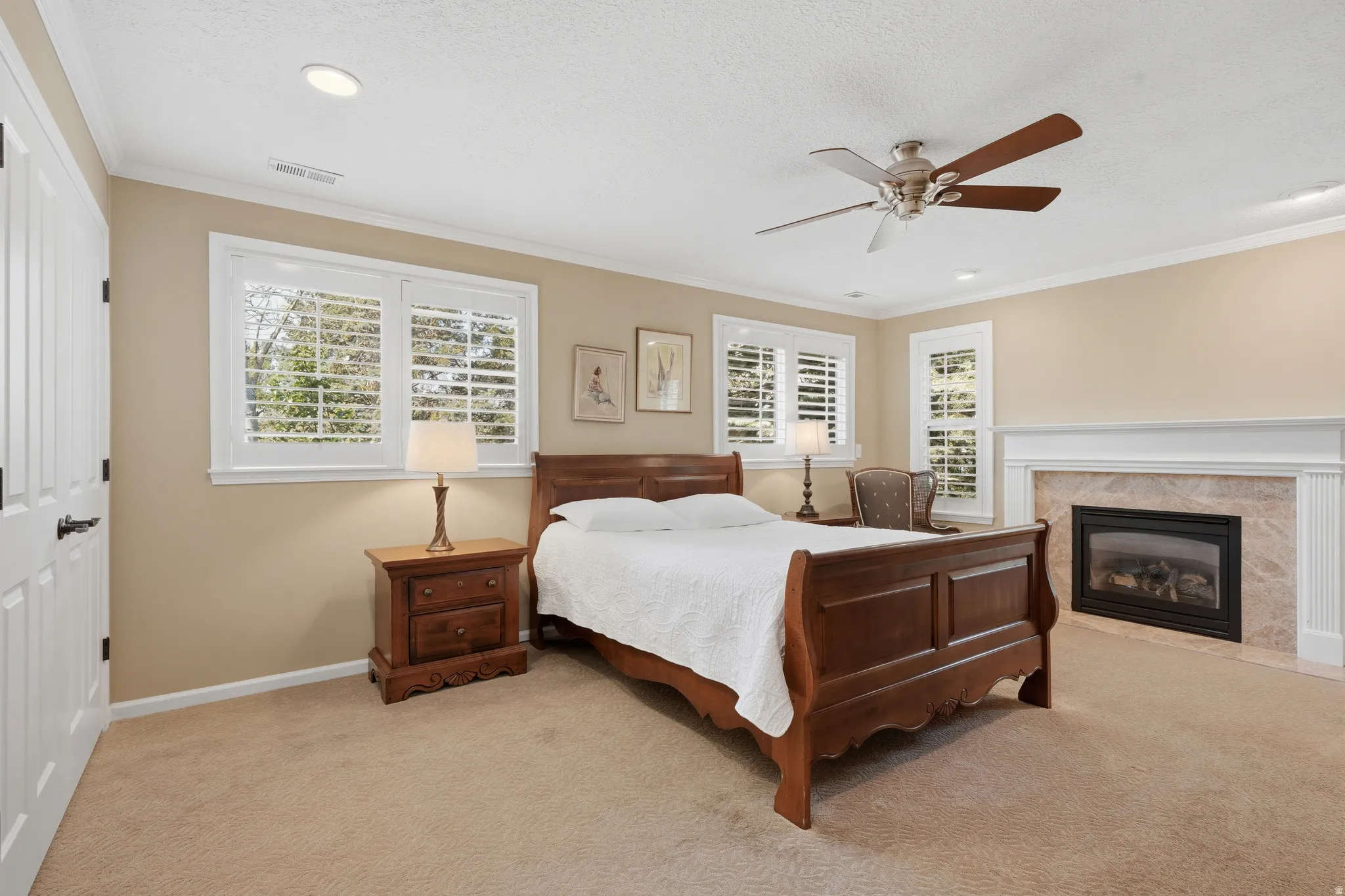 Bedroom featuring a gas fireplace with a stone surround and white mantelpiece, recessed lighting, a ceiling fan, and multiple windows with white plantation shutters