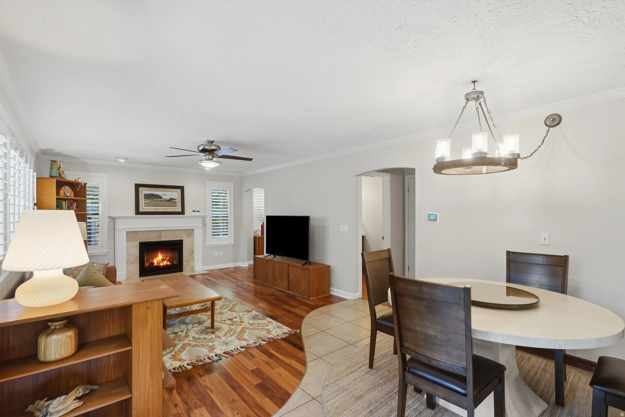 Living area featuring a fireplace with a white mantelpiece and neutral tile surround, wood-finish flooring, and white plantation shutters