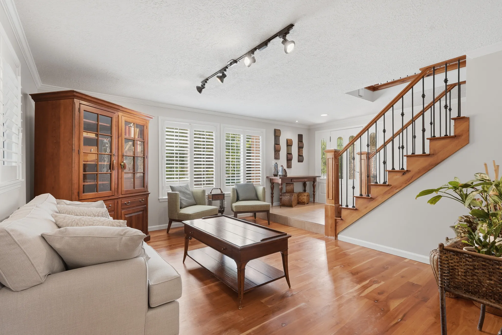 Living area featuring wood-finish flooring, white plantation shutters, and track lighting