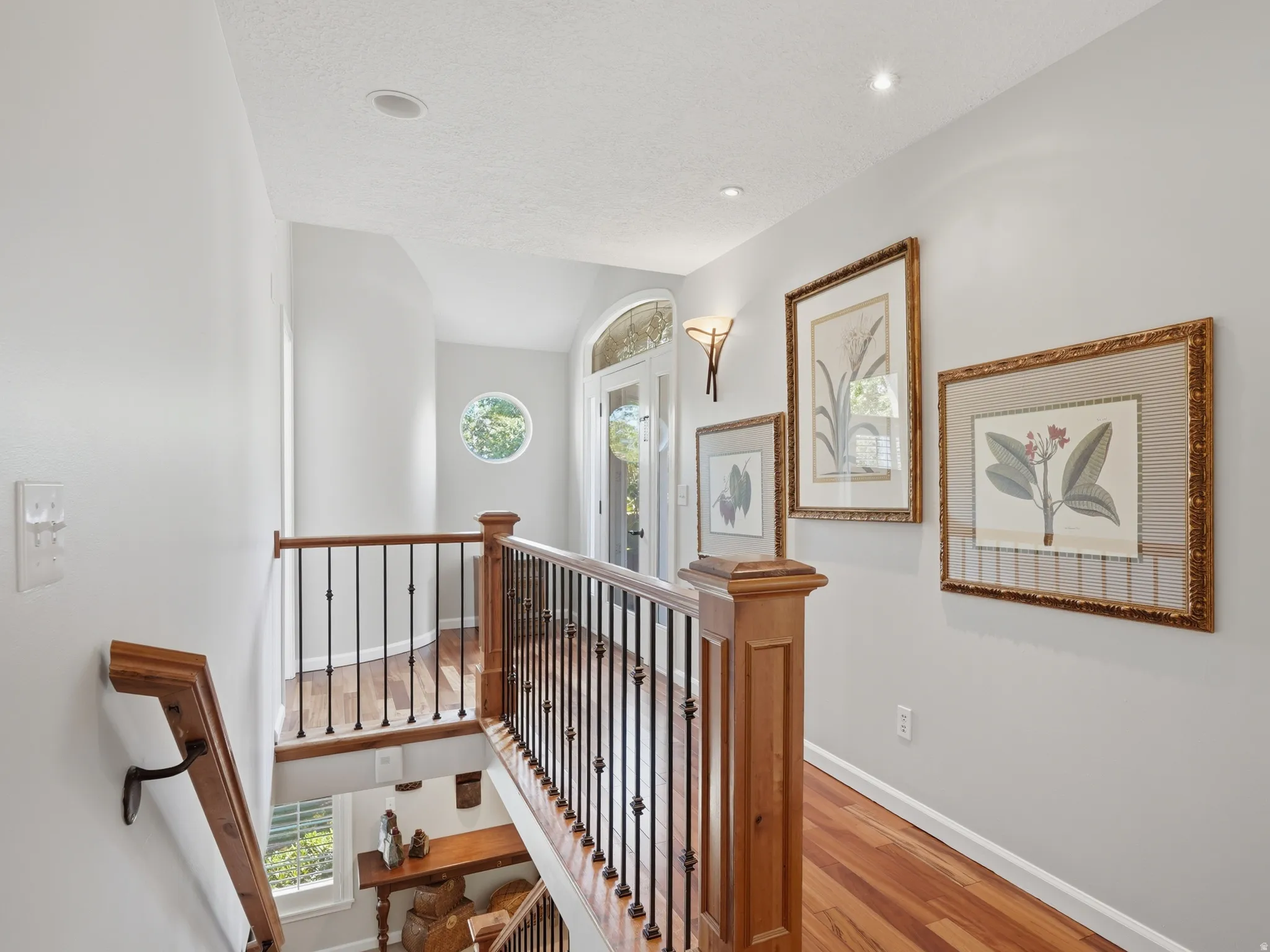 Wood-finish flooring throughout the hallway and landing, complemented by a wood and wrought iron staircase railing