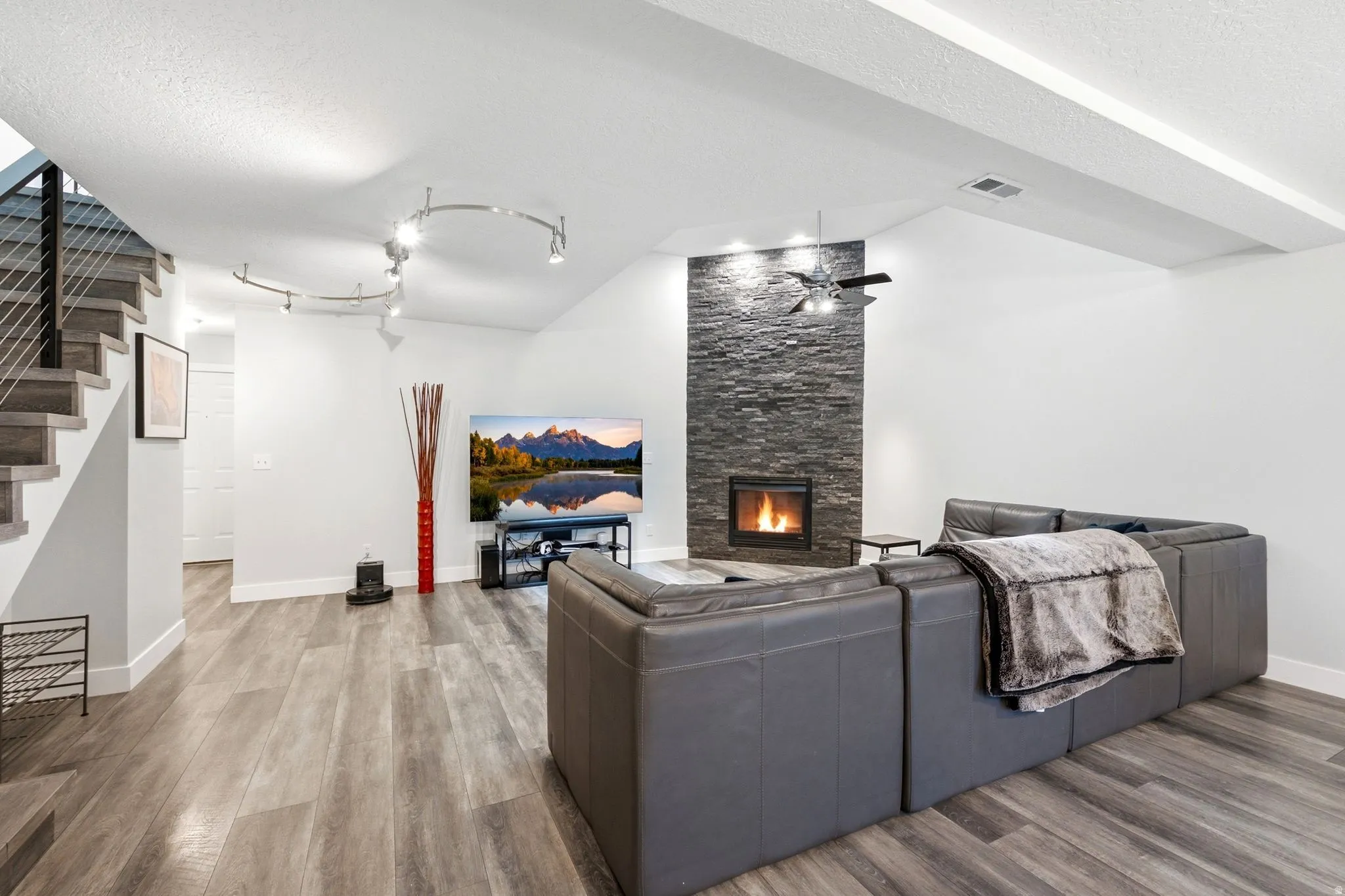 Living area featuring a floor-to-ceiling stacked stone fireplace with an inset firebox, wood-finish flooring, and a contemporary staircase with metal cable railings