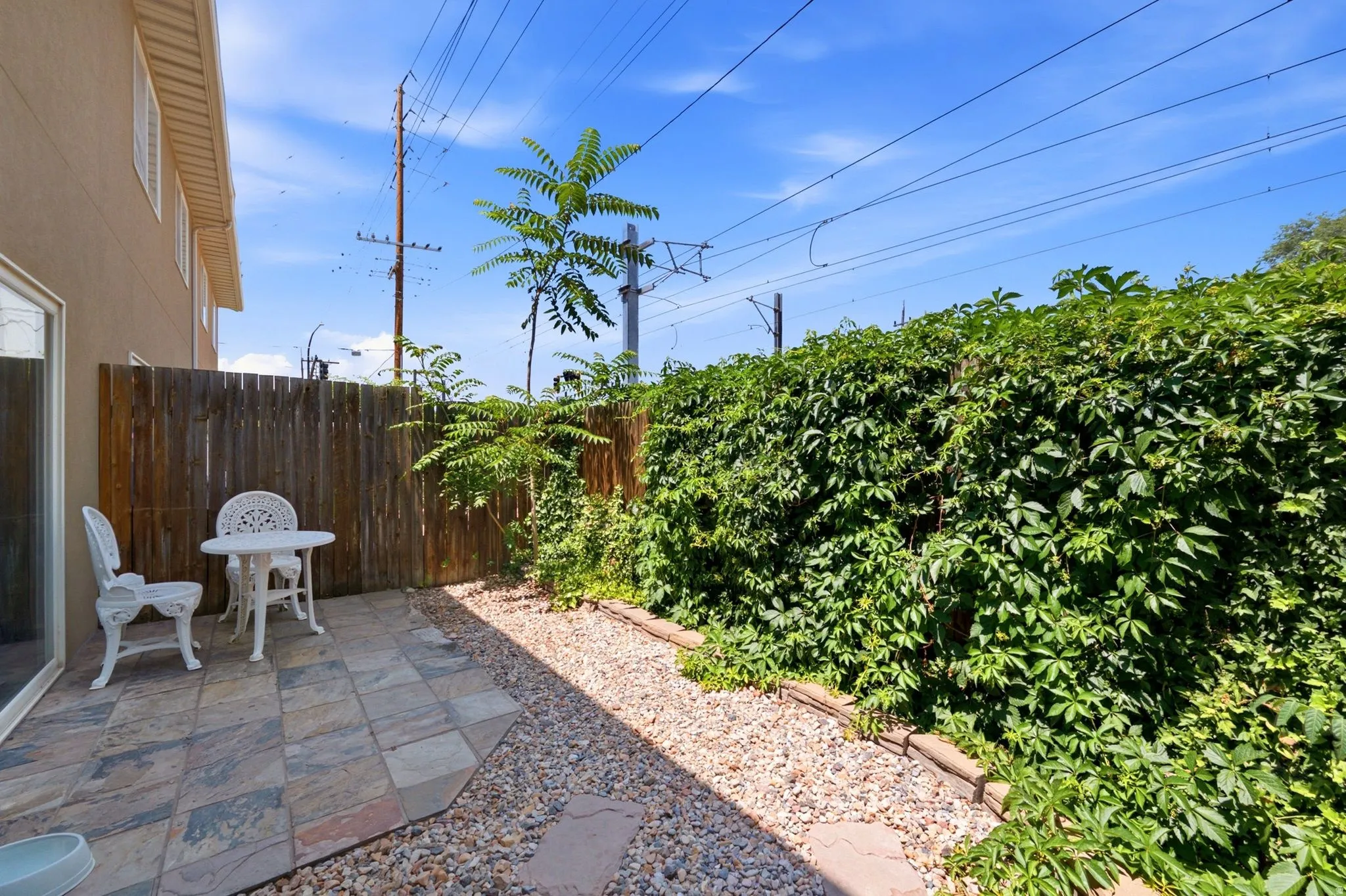 Private patio area featuring stone tile paving, a gravel path, a wood privacy fence, and a lush green ivy-covered wall