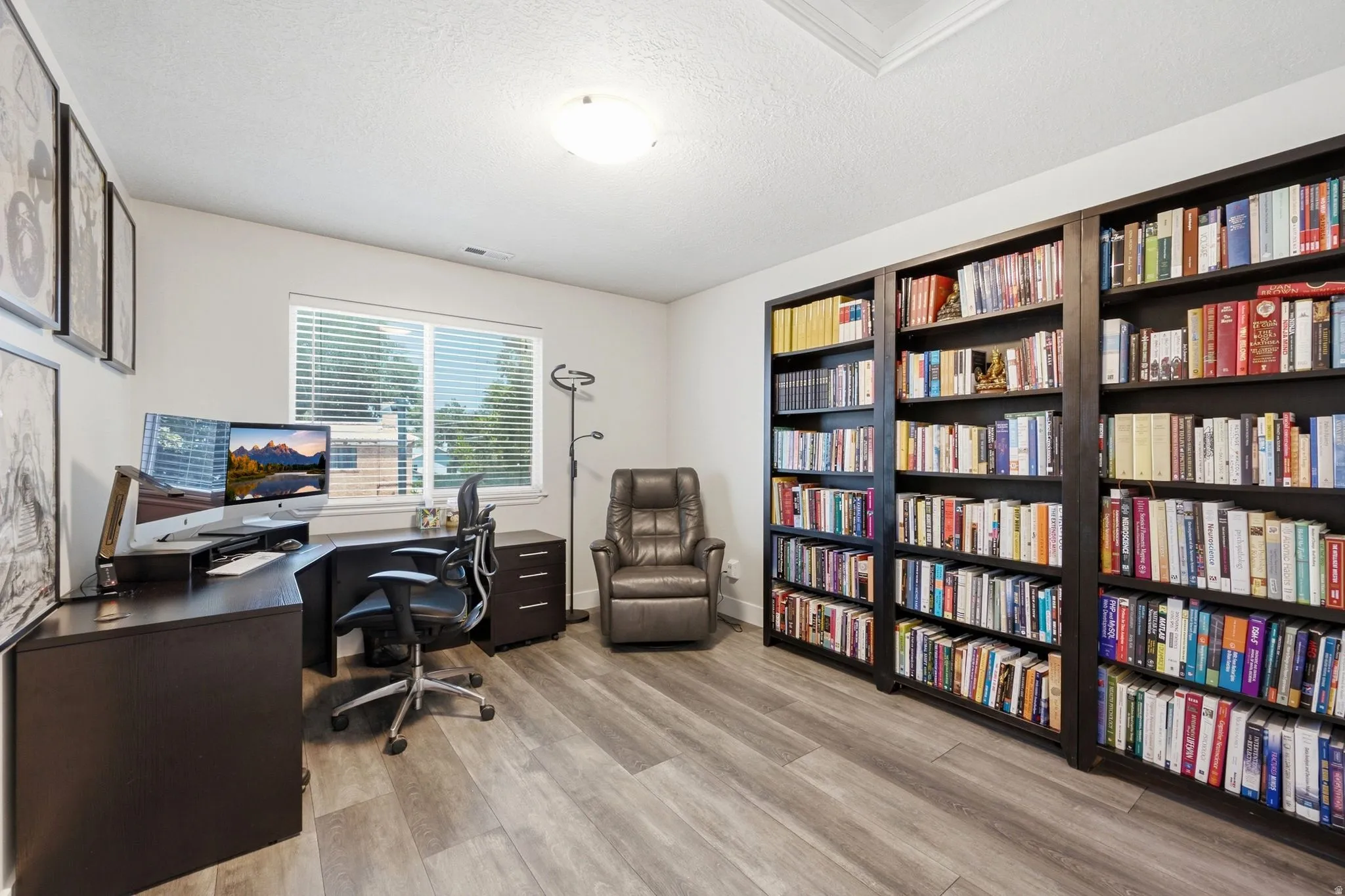 Dedicated office space featuring extensive built-in shelving, wood-finish flooring, a window with blinds, and recessed lighting