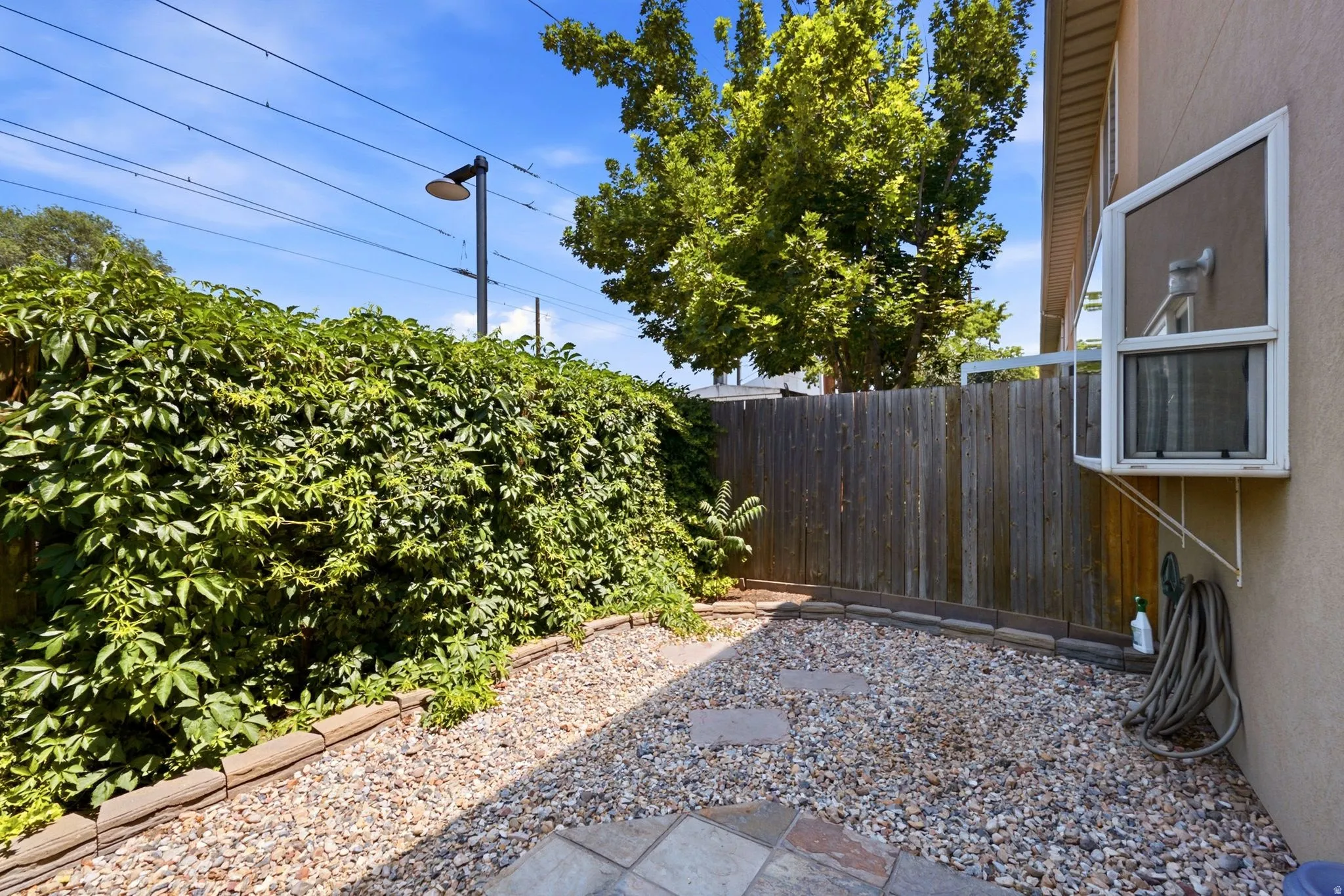 Private patio area featuring a gravel surface with stepping stones, a full privacy fence, and mature perimeter greenery