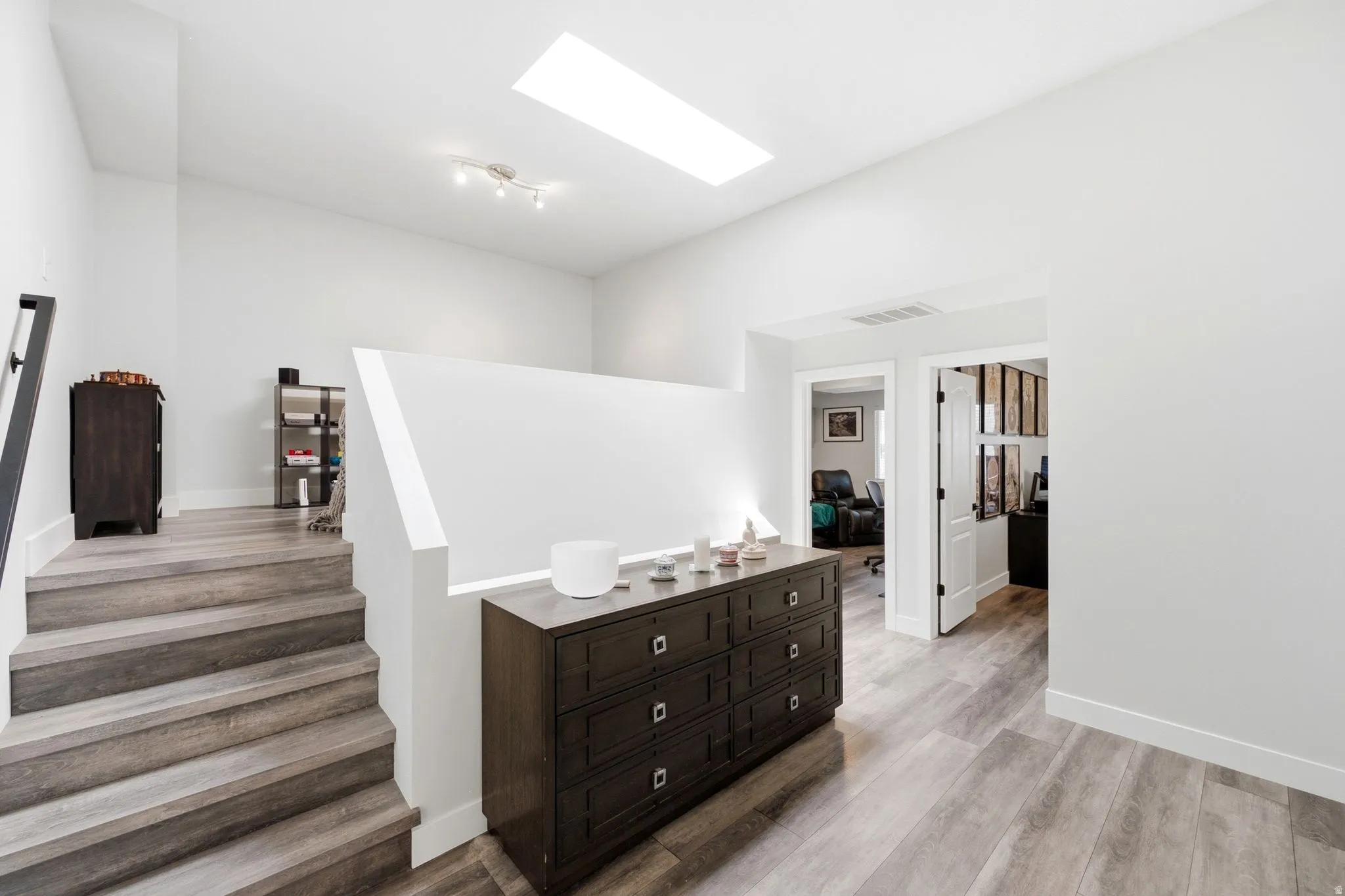 Upper landing featuring a skylight, light wood-finish flooring, white walls, and a modern track light fixture
