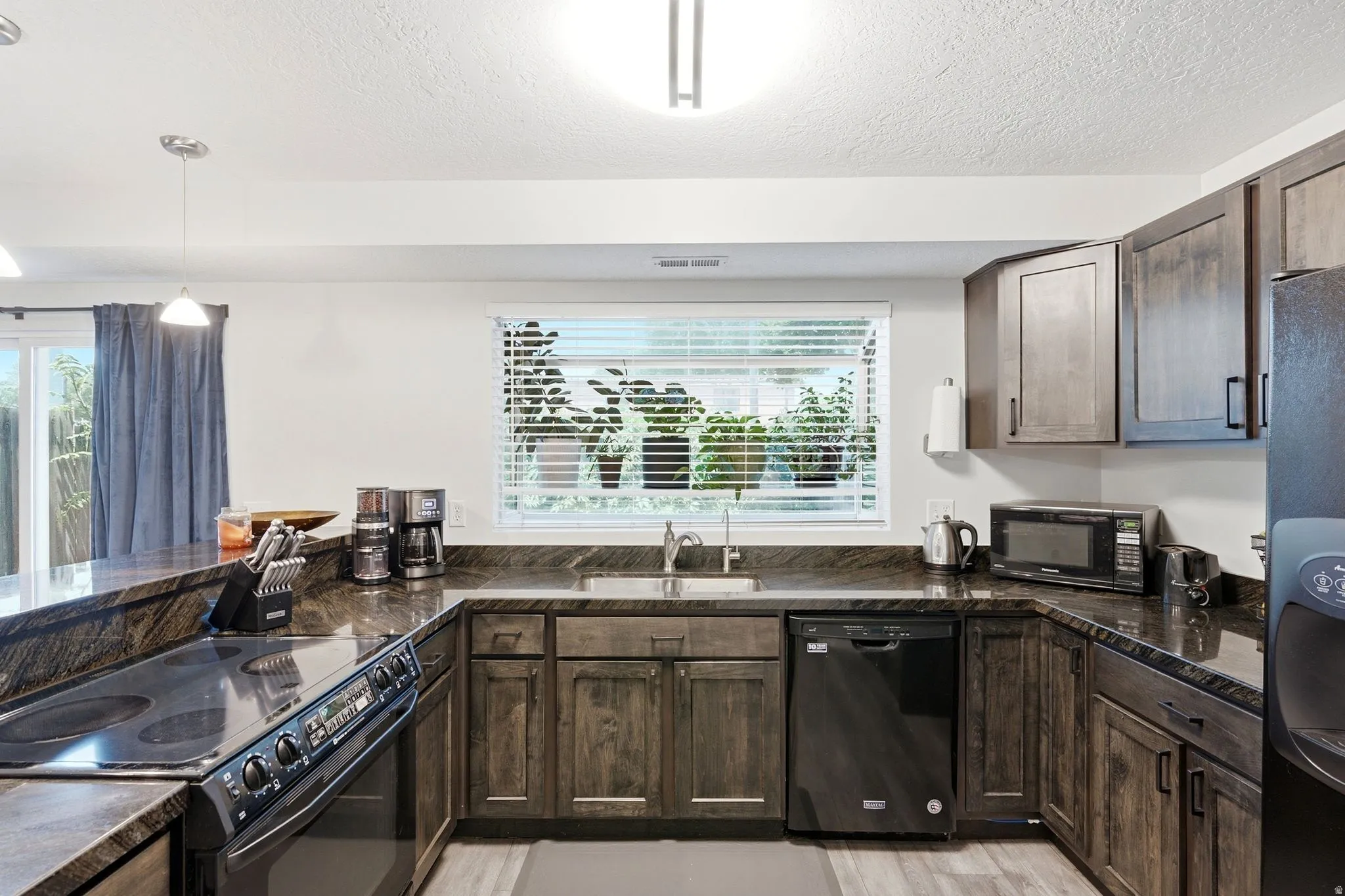 U-shaped kitchen featuring wood-finish cabinetry, dark countertops, and black appliances including a dishwasher and range