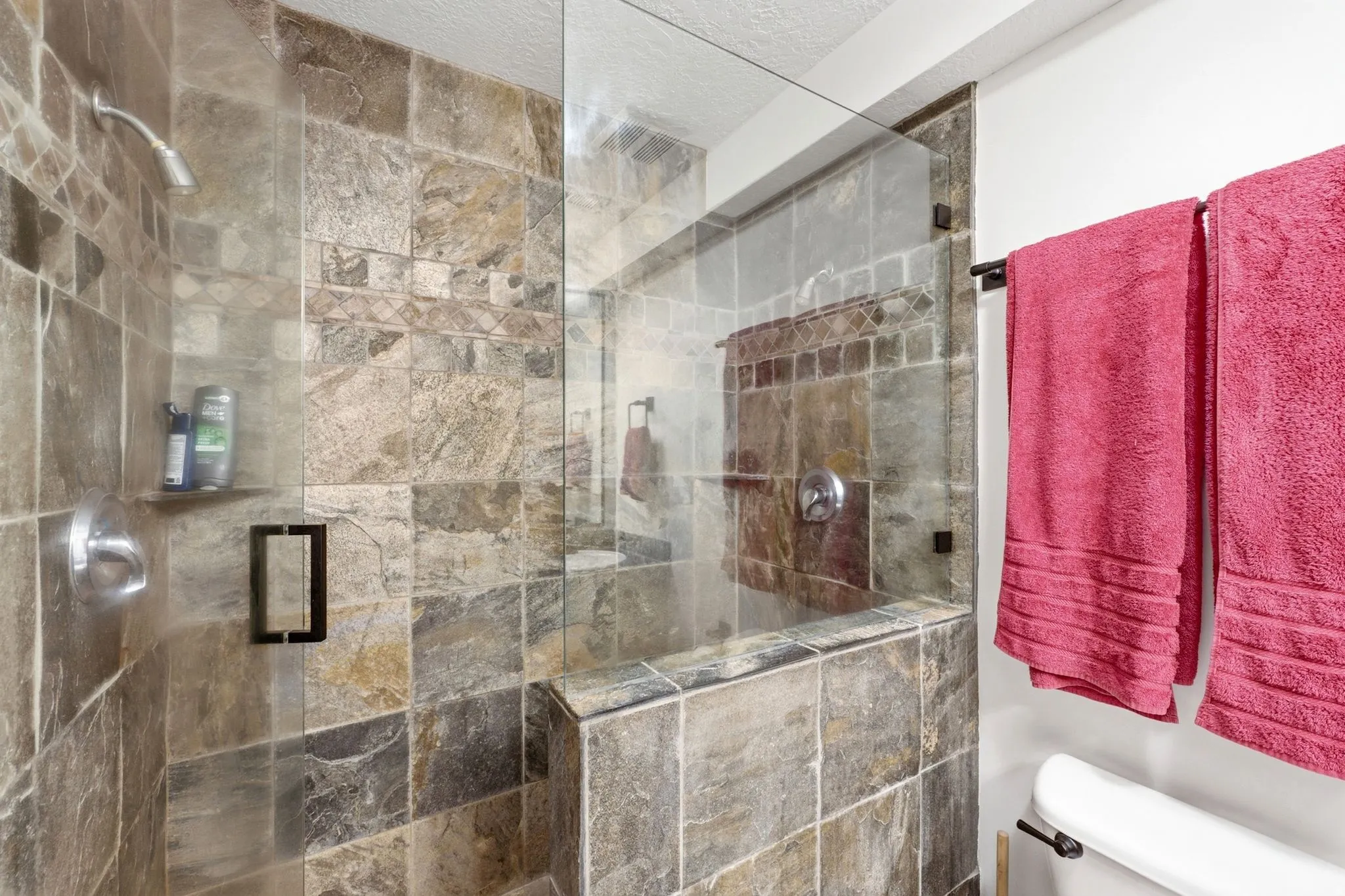 Glass-enclosed shower featuring natural stone-look tile walls, a built-in shower niche, and a tiled shower bench