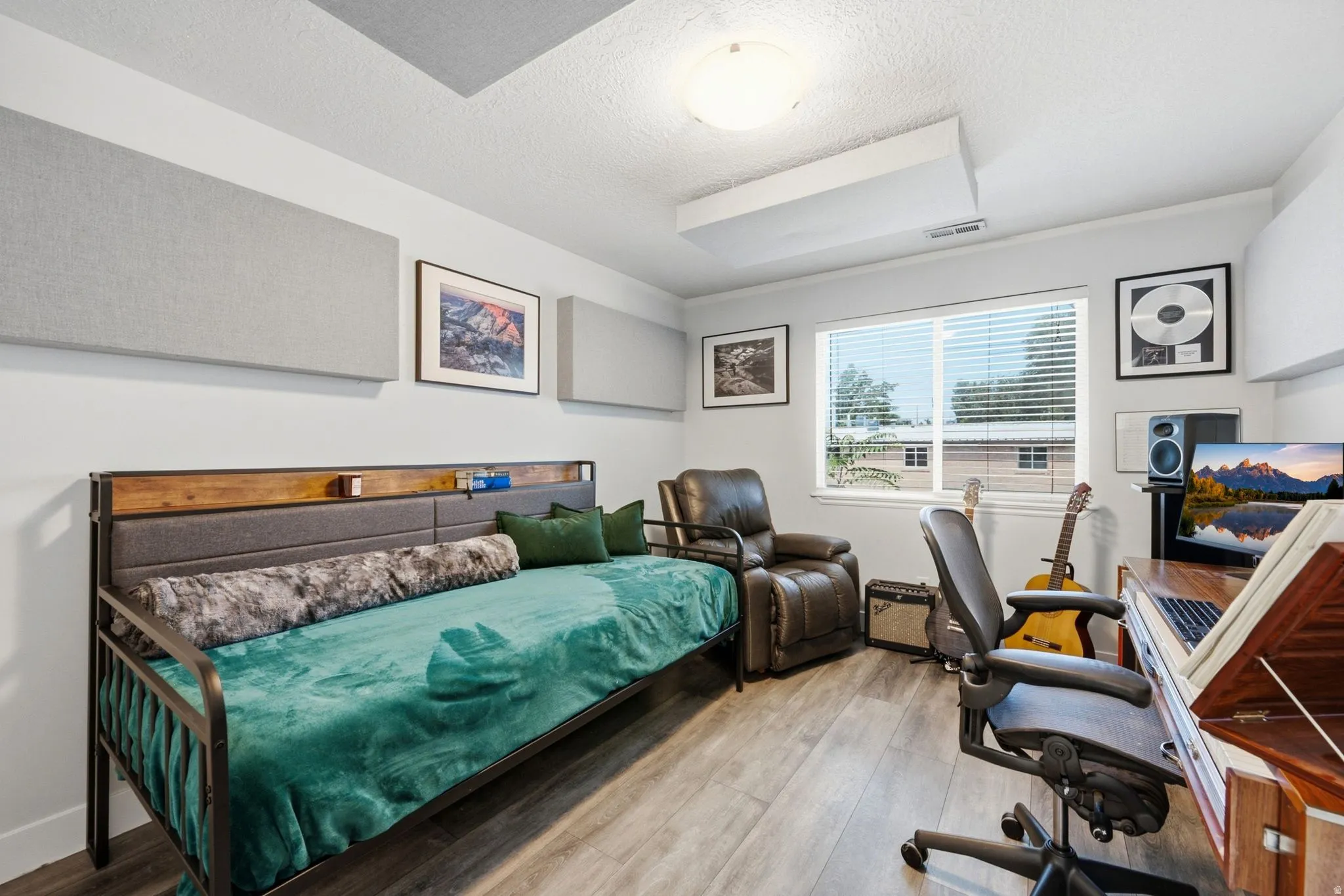 Versatile room featuring wood-finish flooring, a large window with horizontal blinds, built-in sound panels, and a flush-mount ceiling light fixture