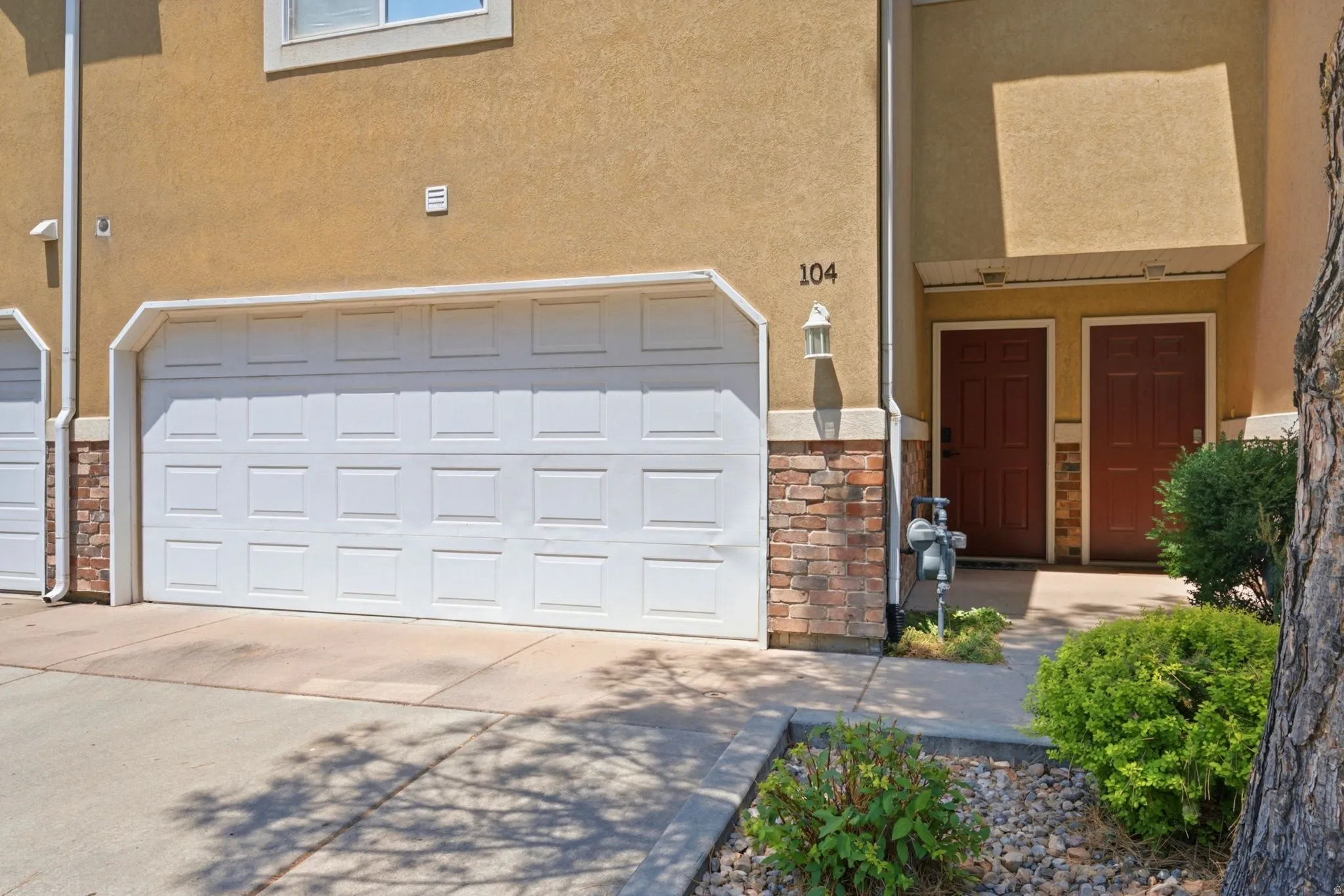 Stucco exterior with brick veneer accents, featuring a paneled garage door and two paneled entry doors