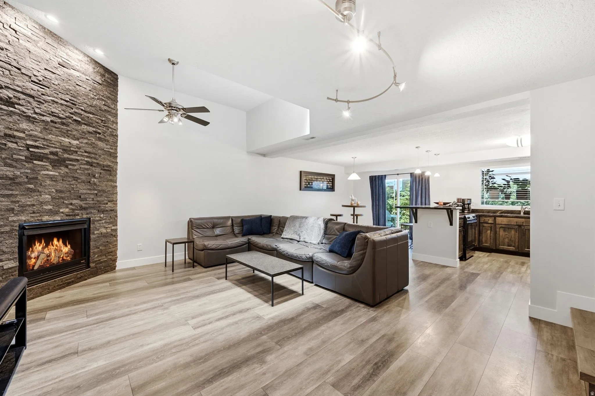 Living area featuring a floor-to-ceiling stone-finish fireplace, wood-finish flooring, vaulted ceiling with a ceiling fan, and track lighting