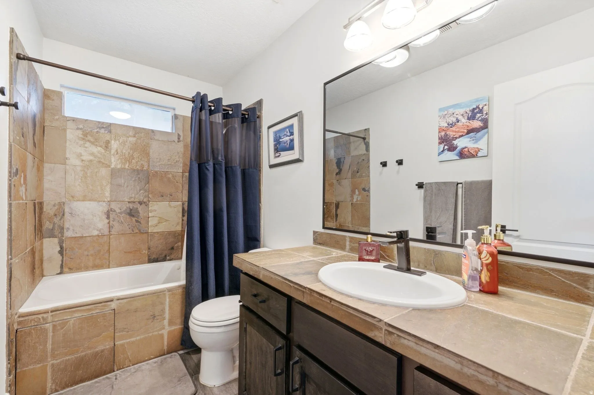Bathroom featuring a tiled shower surround, built-in bathtub, window, dark wood-finish vanity with an integrated sink, and an expansive vanity mirror