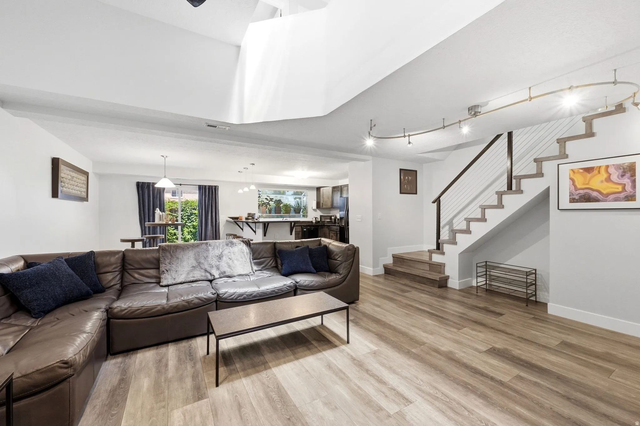 Spacious lower level featuring wood-finish flooring, a modern open-tread staircase with cable railing, track lighting, and recessed ceiling lights