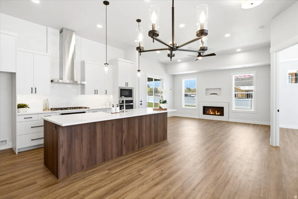 Open-concept living space featuring a modern kitchen island with wood-finish paneling and white countertop, white shaker cabinetry, stainless steel appliances, and wood-finish flooring
