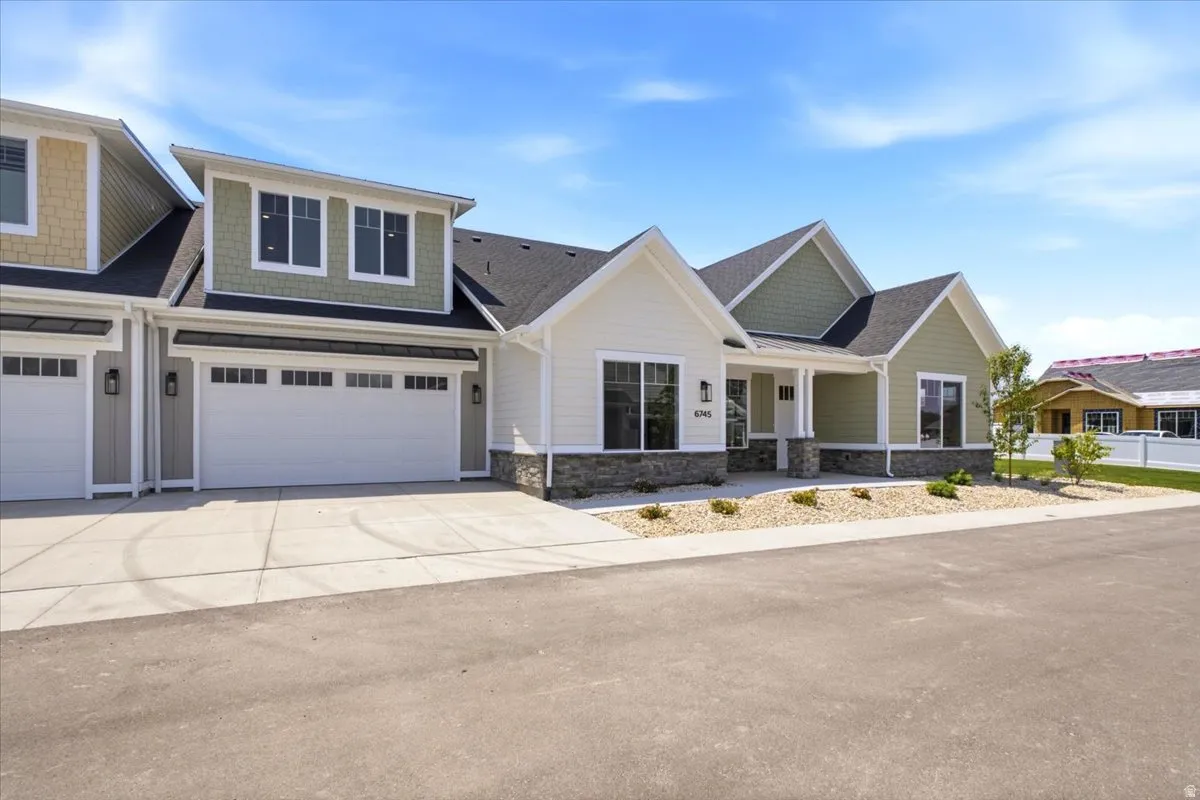 Contemporary townhome exterior featuring an attached two-car garage, stone accent siding, vertical and horizontal siding, and a covered entry porch