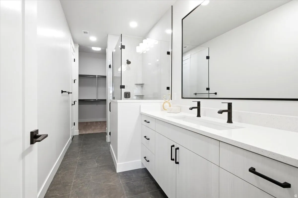 Contemporary bathroom featuring a double vanity with stone countertops and matte black fixtures, a glass-enclosed shower, and a walk-in closet with built-in shelving