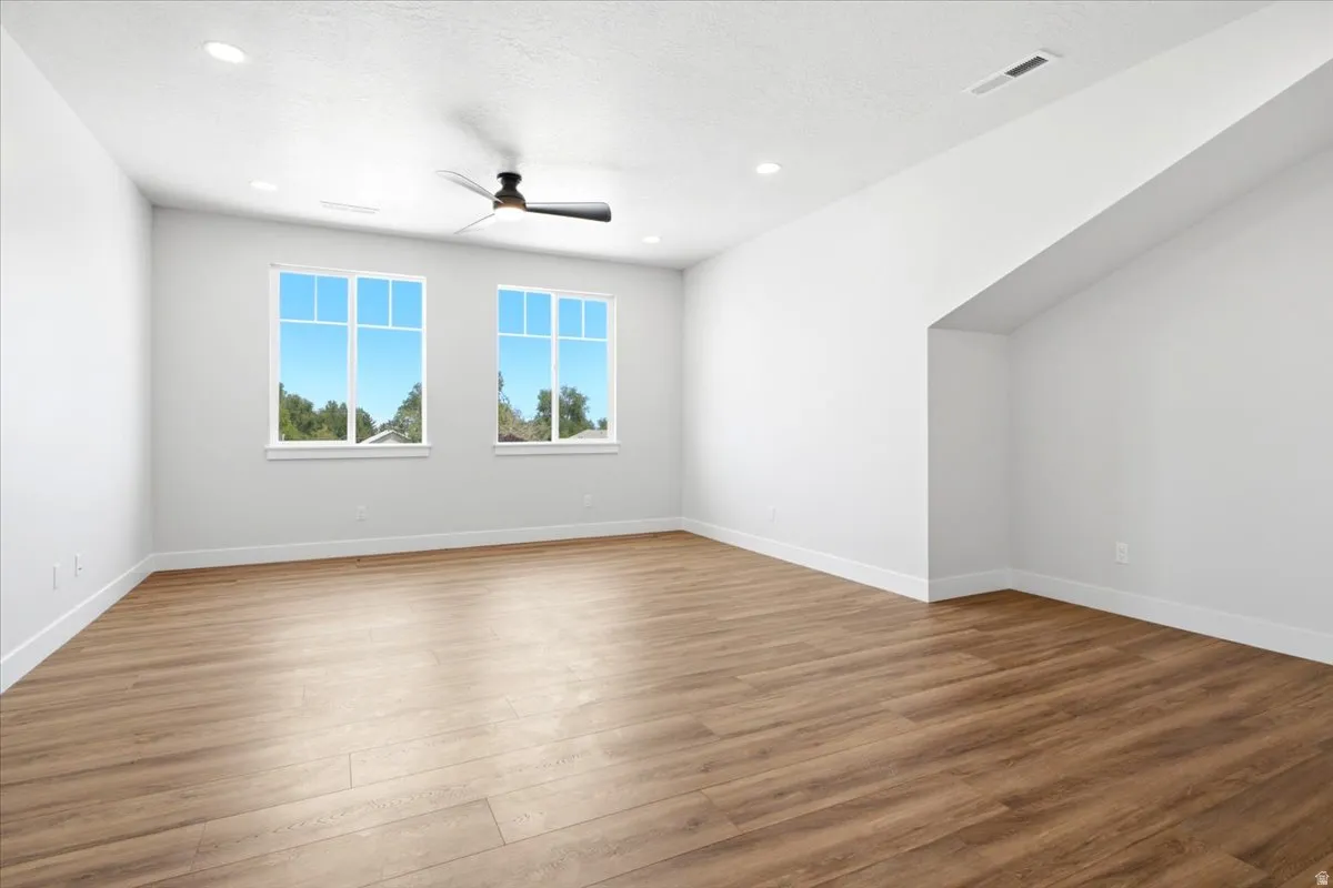 Spacious room featuring wood-finish flooring, two large windows, a ceiling fan, recessed lighting, and crisp white walls