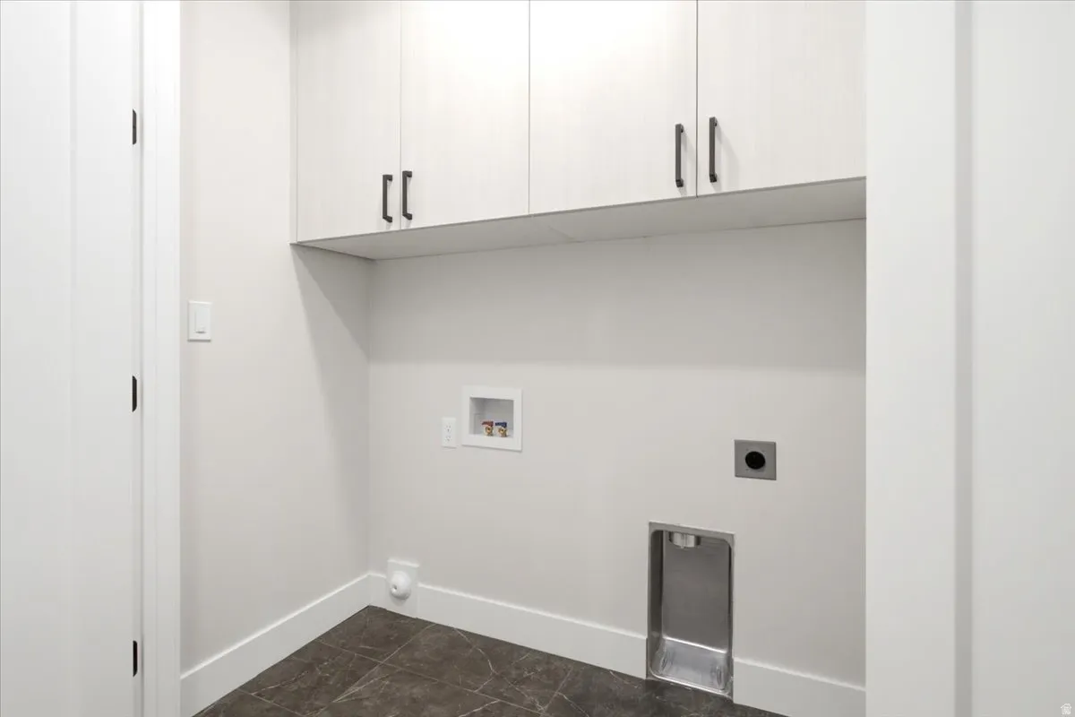 Dedicated laundry area featuring overhead cabinetry with dark hardware, a built-in drain, and connections for appliances
