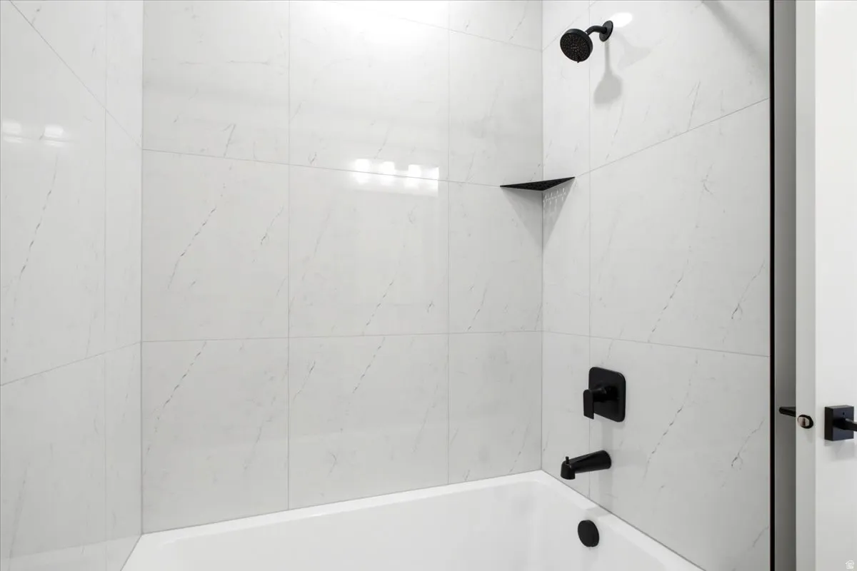 White subway tile surround with black fixtures, including a shower head, faucet, and a built-in corner shelf