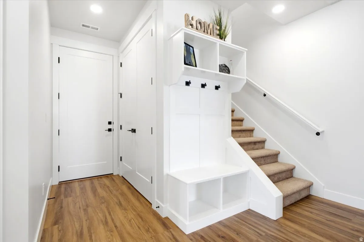 Entryway featuring wood-finish flooring, crisp white walls, and a built-in mudroom unit with storage, bench seating, and coat hooks