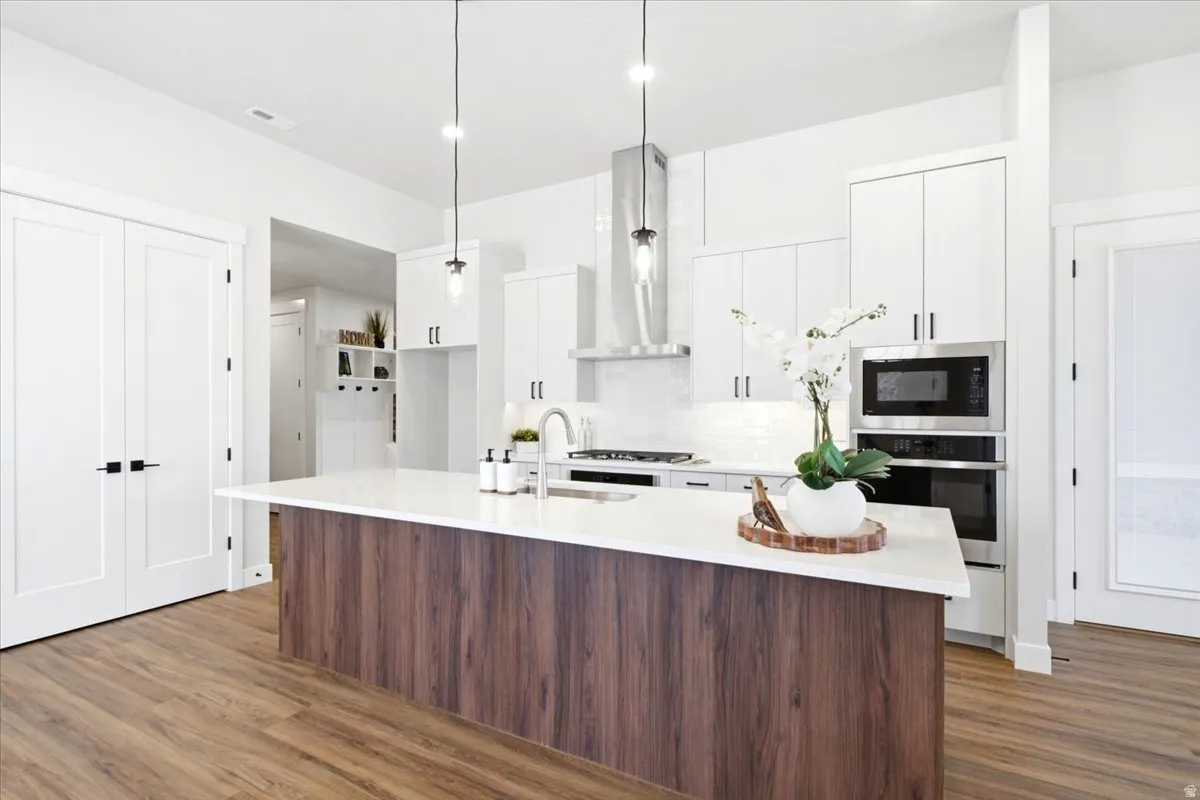 Modern kitchen featuring a wood-finish island with a white countertop, stainless steel appliances, white cabinetry, and wood-finish flooring