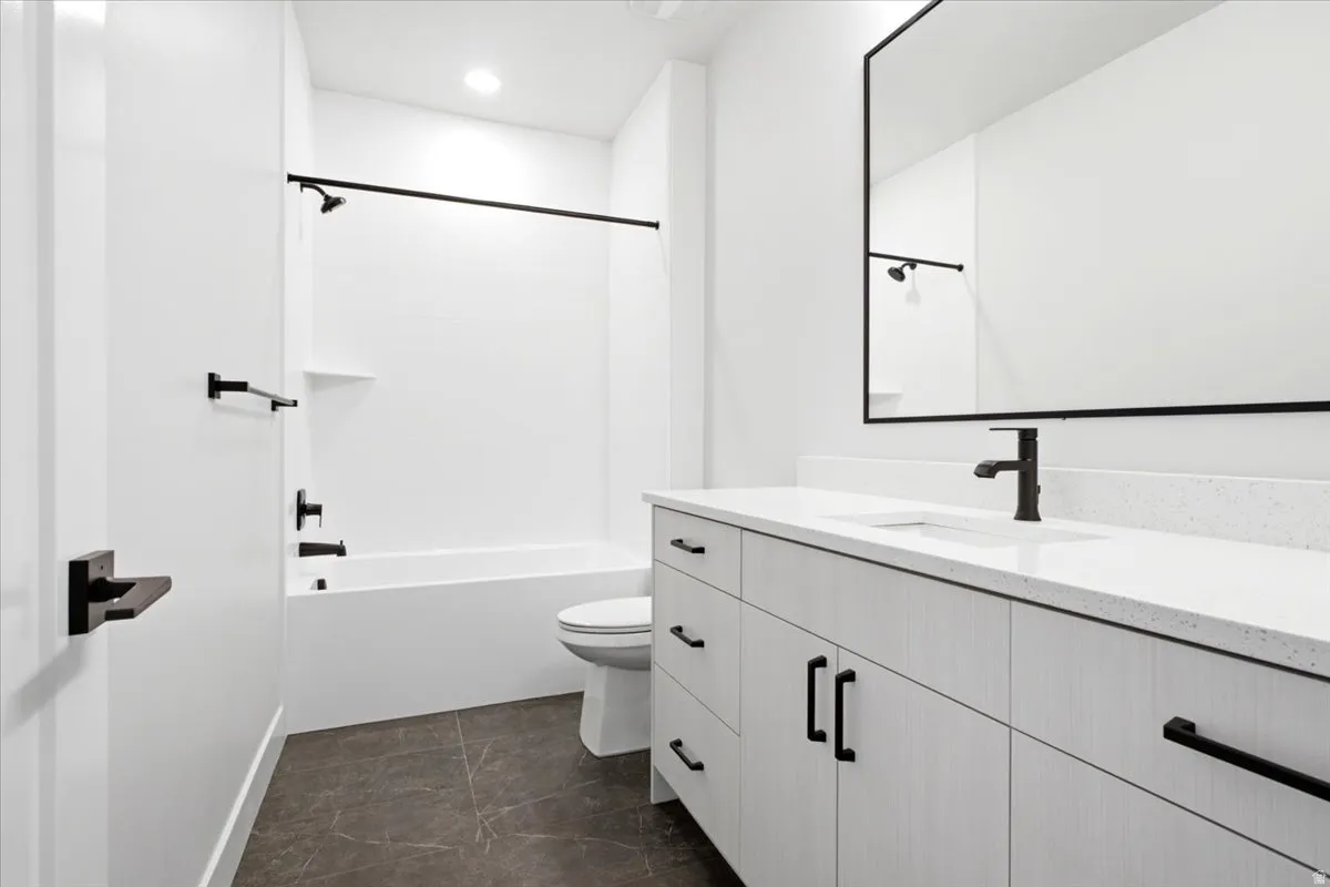 Modern bathroom featuring a white vanity with a light-toned countertop, a large framed mirror, and a white tub/shower combination with matte black fixtures