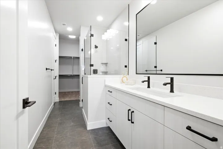 Contemporary bathroom featuring a double vanity with stone countertops and matte black fixtures, a glass-enclosed shower, and a walk-in closet with built-in shelving