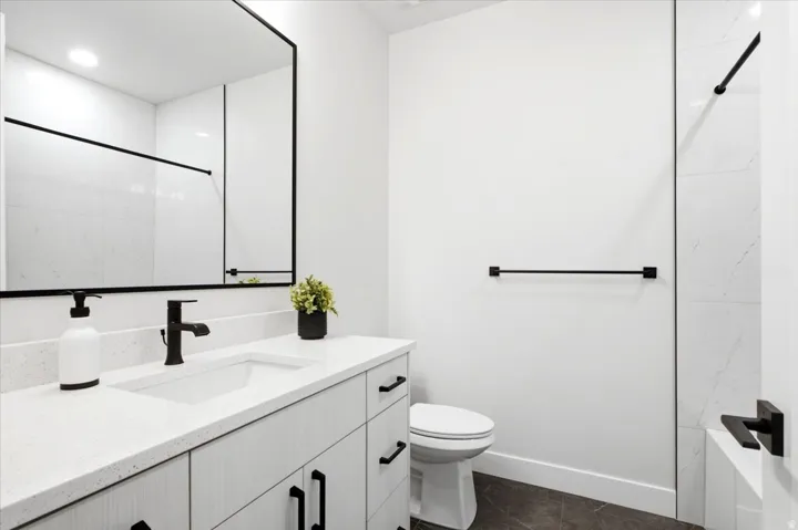 Contemporary bathroom featuring a light wood-finish vanity with quartz countertop, integrated rectangular sink, and matte black hardware
