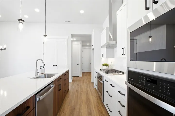 Modern kitchen featuring white shaker cabinetry, wood-finish flooring, stainless steel appliances, a white quartz island with an undermount sink, and black hardware accents