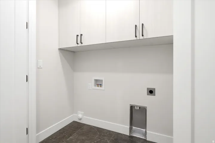Dedicated laundry area featuring overhead cabinetry with dark hardware, a built-in drain, and connections for appliances