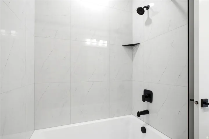 White subway tile surround with black fixtures, including a shower head, faucet, and a built-in corner shelf