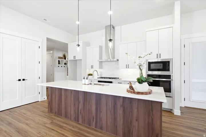 Modern kitchen featuring a wood-finish island with a white countertop, stainless steel appliances, white cabinetry, and wood-finish flooring