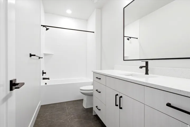 Modern bathroom featuring a white vanity with a light-toned countertop, a large framed mirror, and a white tub/shower combination with matte black fixtures