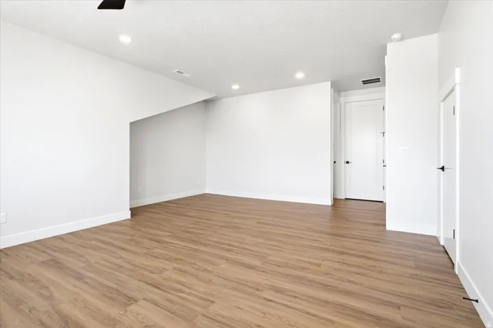 Spacious interior room featuring wood-finish flooring, recessed lighting, and crisp white walls