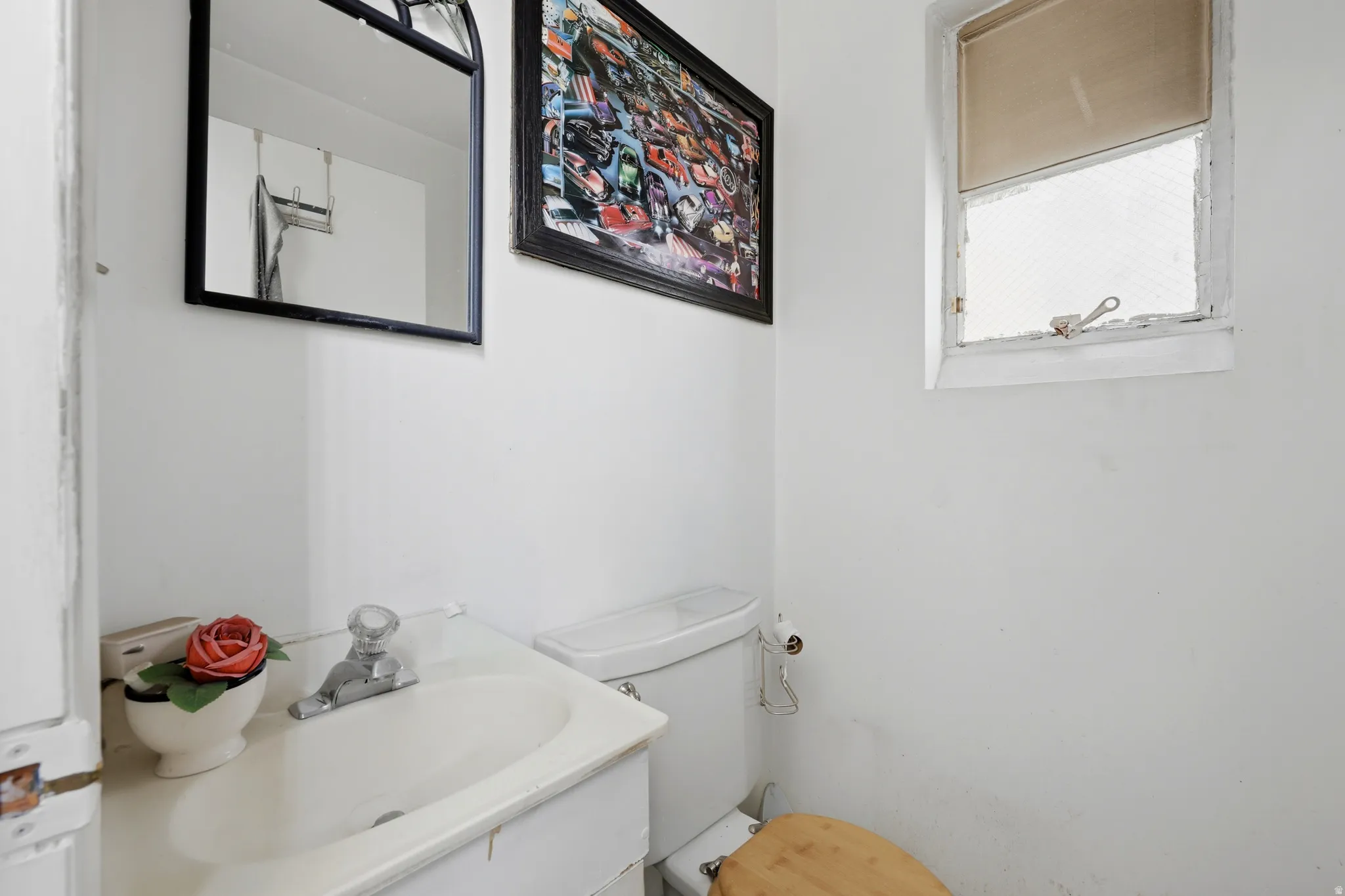 White bathroom featuring a vanity with integrated sink, a toilet, a small window, and a wall-mounted mirror