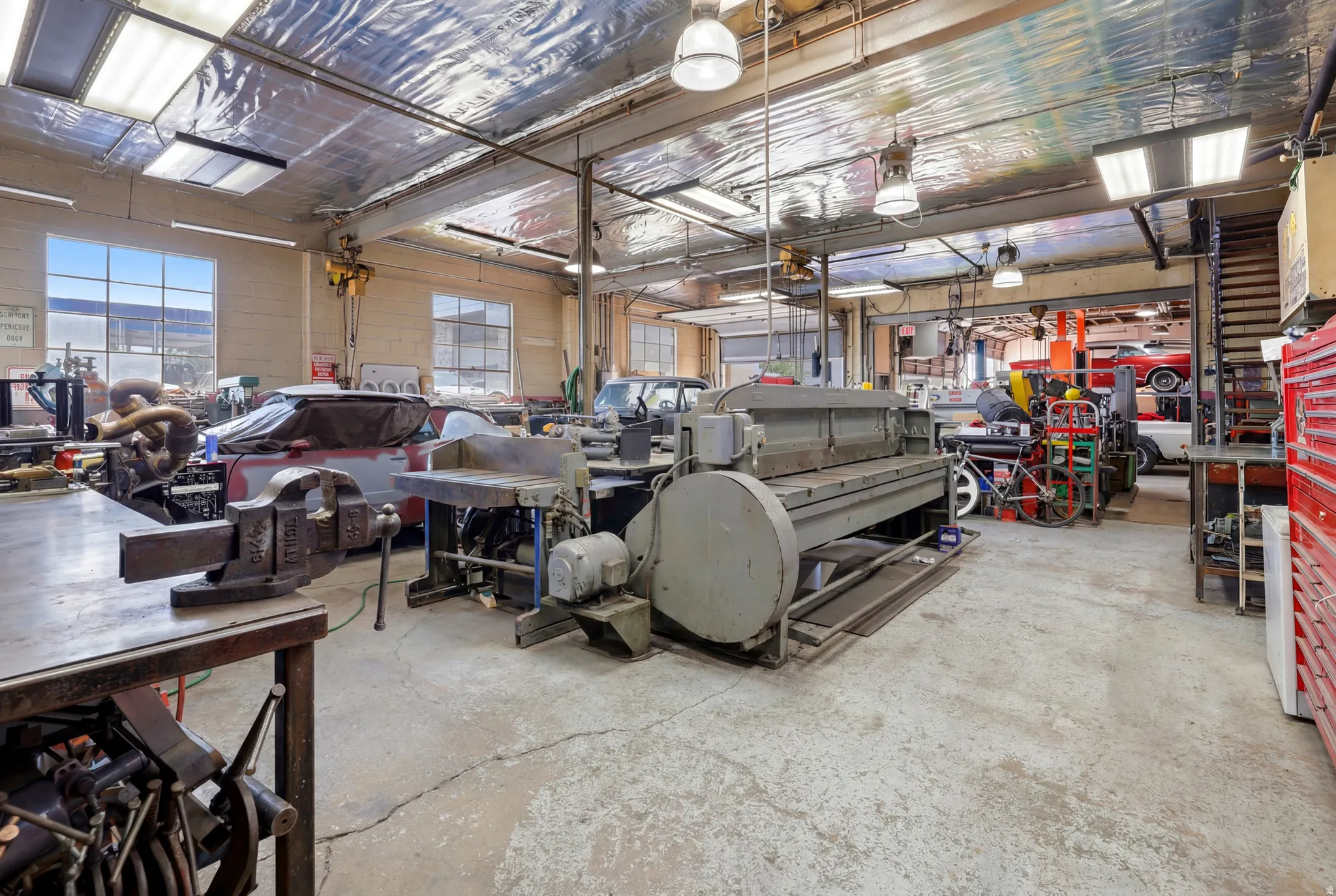 Spacious workshop featuring concrete flooring, expansive windows, overhead lighting, and exposed structural elements