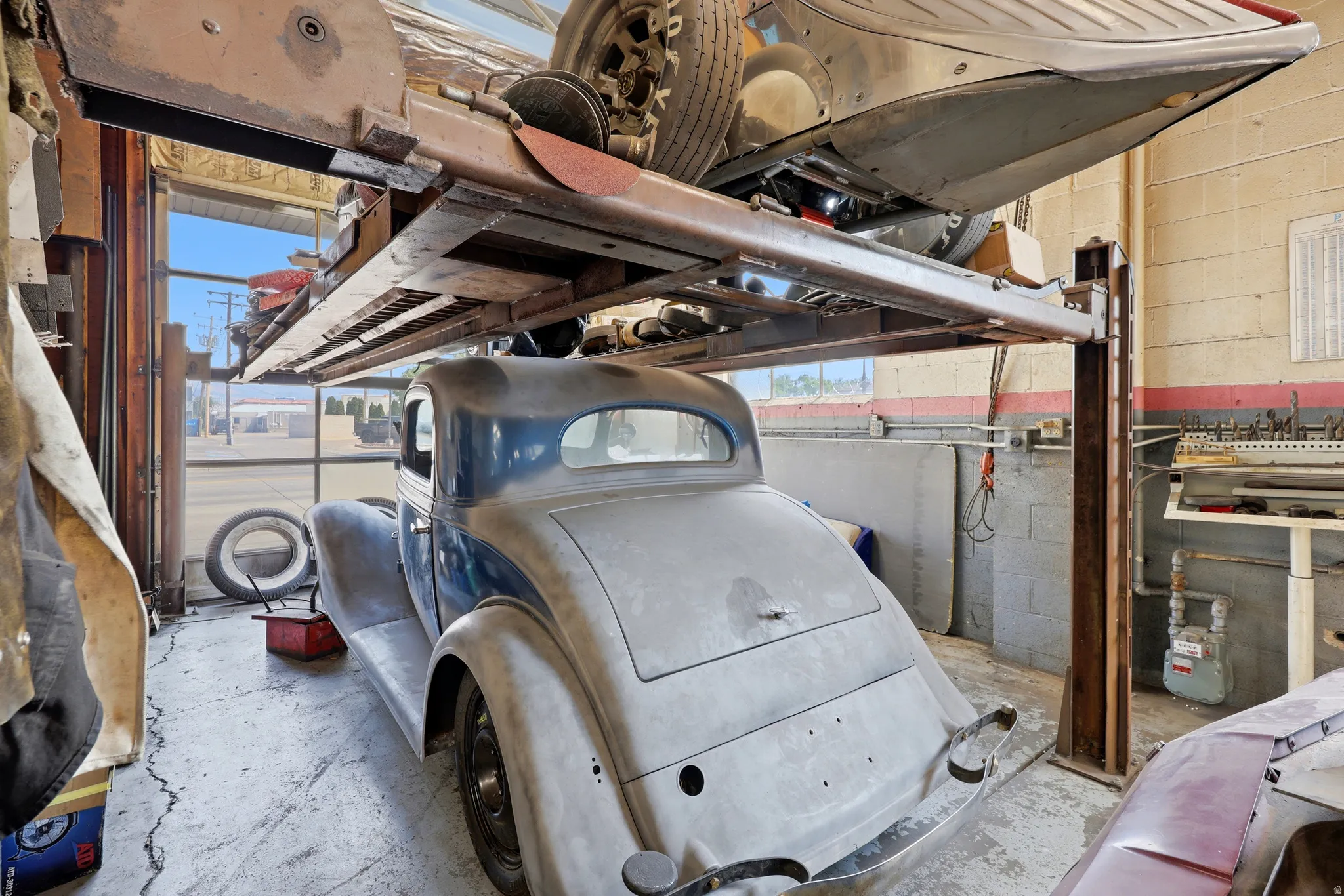 Automotive service bay featuring a hydraulic lift system, concrete flooring, exterior-facing windows, and block wall construction